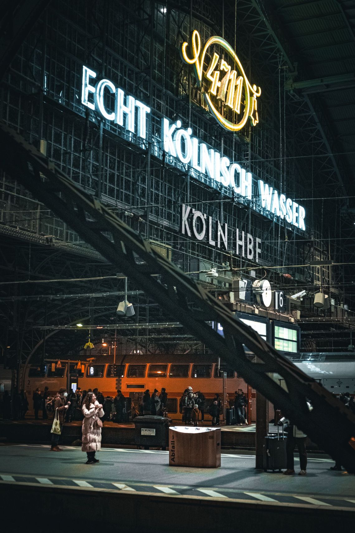 Bild von einem Bahnsteig an dem eine Frau steht. Im Hintergrund ist das große 4711 Logo als Lichtinstallation zu sehen.