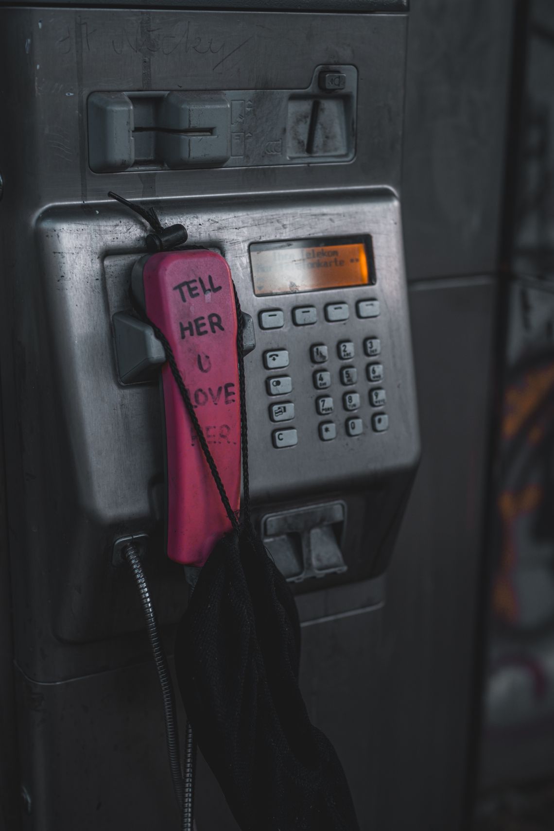 Ein Bild eines pinken Telefonhörers in einer alten Telekom-Telefonzelle. Auf dem Hörer steht "Tell her u love her".